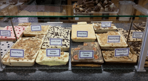 A display of various fudge flavors, including pecan praline, lemon meringue, and cookie dough, with labels.