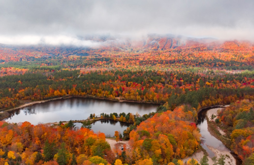 Aerial view of a vibrant autumn landscape with colorful trees surrounding a serene lake and misty mountains in the background.