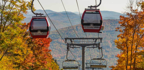 Two red gondolas on a ski lift surrounded by vibrant autumn foliage and mountains in the background.