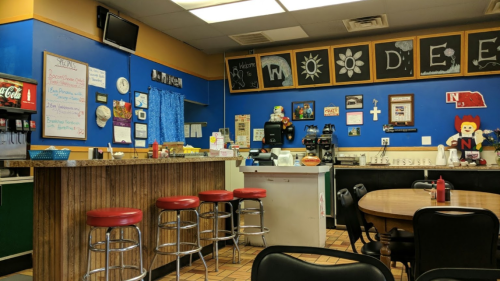 A colorful diner interior with a bar, tables, and decor featuring flowers and a clown, creating a cheerful atmosphere.