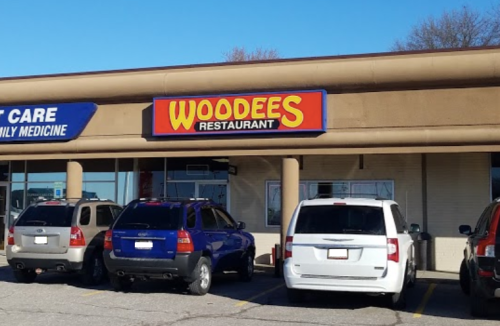 Exterior of a restaurant named "Woodees" with parked cars in front, located in a shopping plaza.