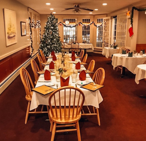 A festive dining room with a decorated Christmas tree, tables set with white tablecloths and red napkins.