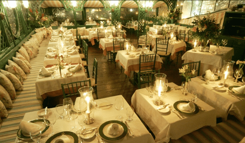 Elegant restaurant interior with candlelit tables, green chairs, and floral decorations, creating a warm ambiance.