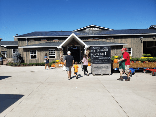 A family approaches an apple barn with pumpkins and flowers outside on a sunny day.