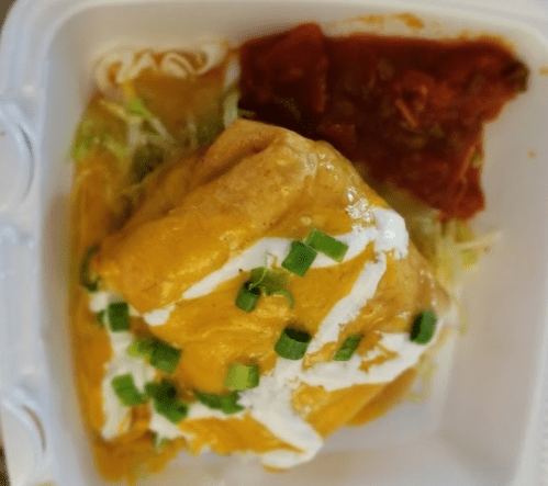 A burrito topped with yellow sauce, sour cream, and green onions, served with a side of red salsa and lettuce.