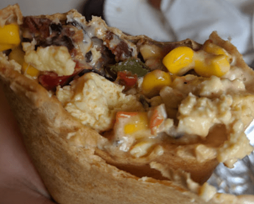 A close-up of a burrito filled with scrambled eggs, corn, peppers, and cheese, partially bitten.