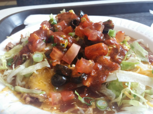 A colorful plate of nachos topped with lettuce, tomatoes, olives, and salsa, served in a casual dining setting.
