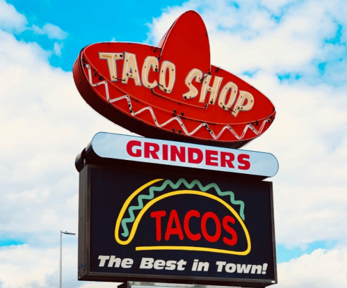 Brightly lit sign for a taco shop featuring a sombrero, with "Grinders" and "The Best in Town!" below.