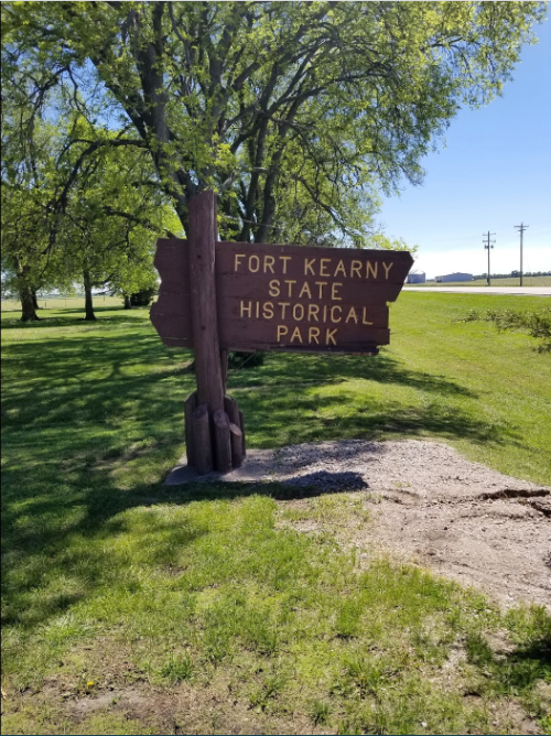 Sign for Fort Kearny State Historical Park, surrounded by green grass and trees on a sunny day.