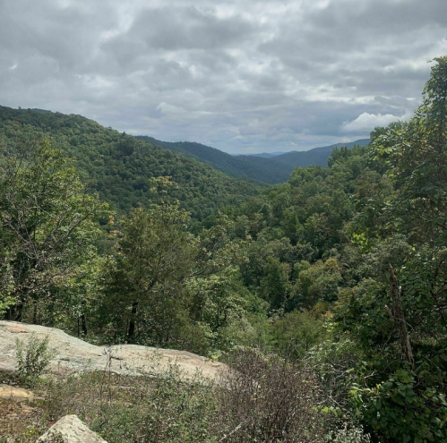 A scenic view of a lush green valley surrounded by mountains under a cloudy sky.