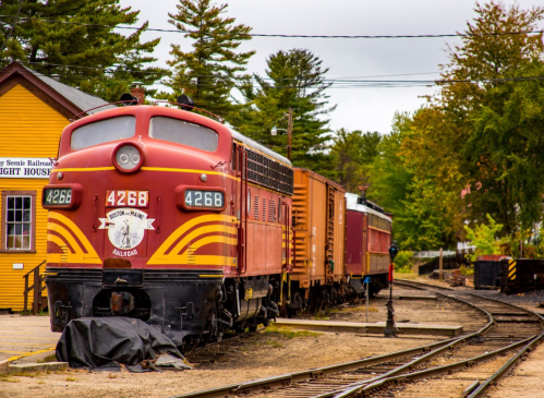 A vintage red train engine with the number 4268 parked beside freight cars in a scenic railway setting.