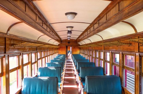 Interior of a vintage train car featuring wooden paneling and rows of green upholstered seats.