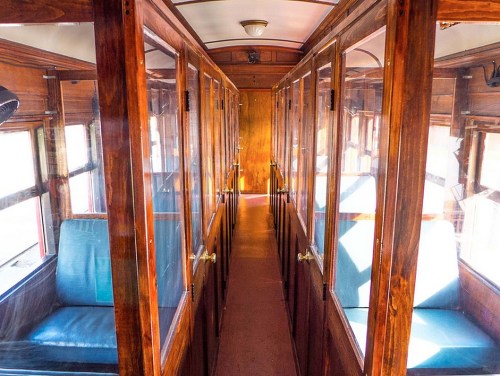 Interior of a vintage train car, featuring wooden paneling and glass-paneled doors along a narrow aisle.