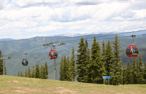 A scenic view of a ski resort gondola lift with mountains and trees in the background under a cloudy sky.