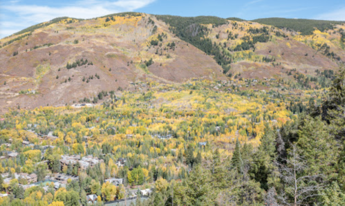 A scenic view of mountains covered in autumn foliage, with a valley of trees and small buildings below.