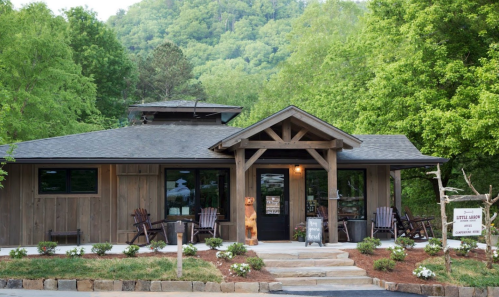 A rustic wooden building surrounded by greenery, featuring a welcoming entrance and outdoor seating.