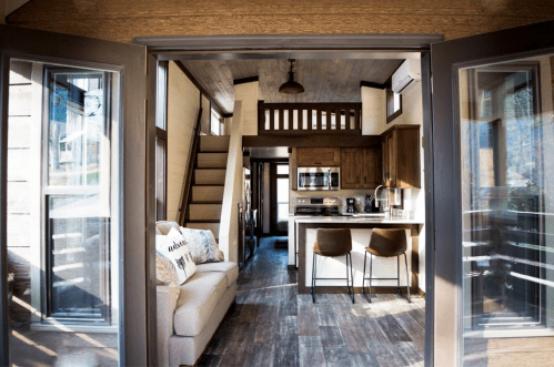 Cozy interior of a modern home, featuring a living area, kitchen, and staircase, with natural light streaming in.