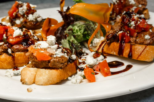 A plate of bruschetta topped with tomatoes, cheese, and balsamic glaze, garnished with salad and carrot ribbons.