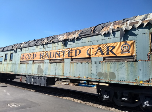 An old train car with a weathered exterior and a banner reading "Old Haunted Car" displayed on the side.