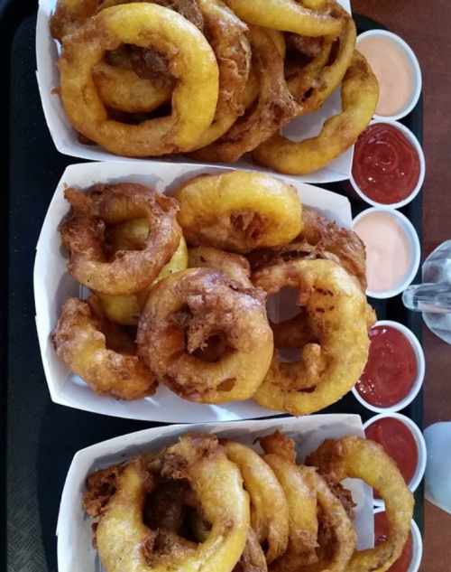 A tray of golden, crispy onion rings served with various dipping sauces in small cups.