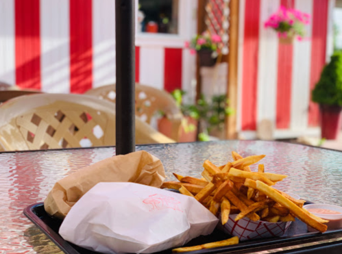 A tray with a wrapped sandwich and a serving of golden fries, set on a glass table with a colorful background.