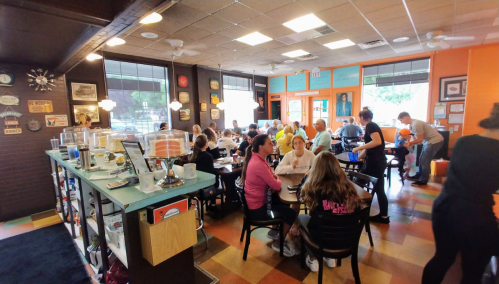 A busy café filled with people dining and socializing, featuring colorful decor and a lively atmosphere.
