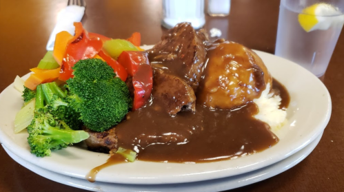 A plate of meatloaf topped with brown gravy, served with mashed potatoes, mixed vegetables, and a glass of water.