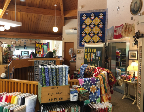 A cozy fabric store interior with colorful quilts, fabric rolls, and a warm, inviting atmosphere.