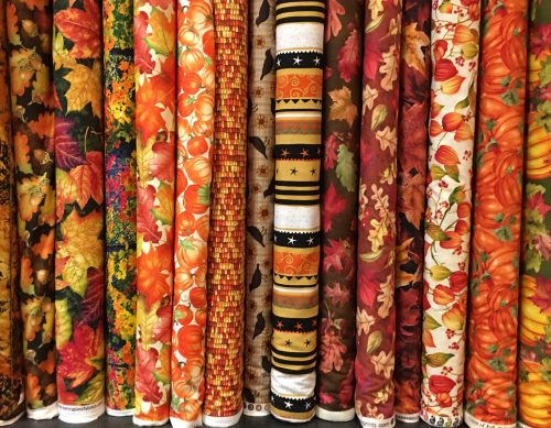A variety of colorful fabric rolls featuring autumn leaves, pumpkins, and seasonal patterns in warm tones.