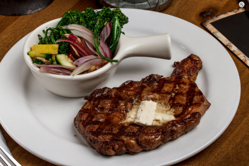 A grilled steak with a pat of butter, served alongside a bowl of mixed vegetables.