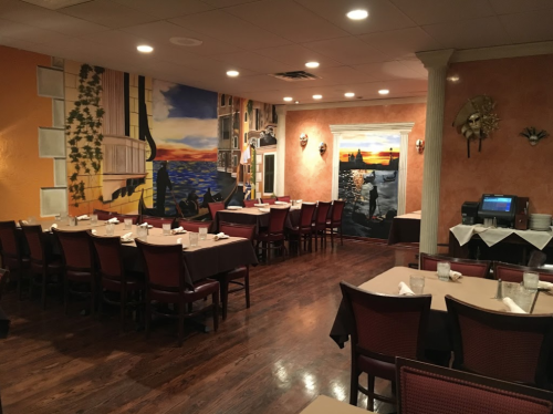 Cozy restaurant interior with wooden floors, tables set for dining, and vibrant wall murals depicting a sunset.