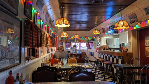 Cozy diner interior with colorful lights, checkered floor, and vintage decor, featuring tables and a counter.