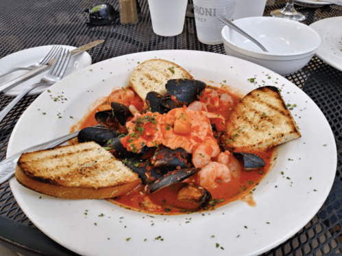 A plate of seafood pasta with shrimp, mussels, and tomato sauce, served with toasted bread on the side.