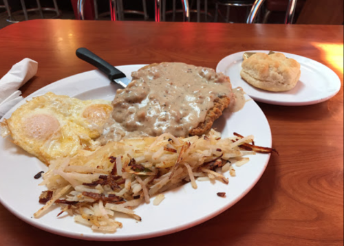 A plate of chicken-fried steak with gravy, two fried eggs, hash browns, and a biscuit on the side.