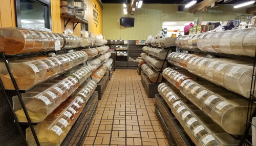 A grocery store aisle lined with clear containers of various spices and herbs on shelves.