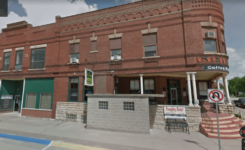 Historic brick building with large windows, a coffee shop sign, and a "No Parking" sign outside.