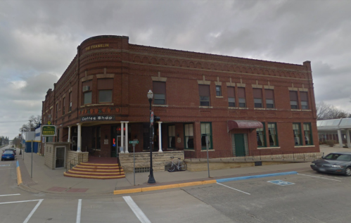 Historic brick building with a coffee shop on the ground floor, featuring large windows and a welcoming entrance.