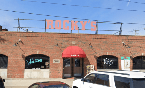 A brick building with a red awning and sign reading "Rocky's," featuring neon signs in the windows.
