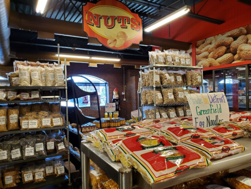 A grocery store aisle filled with various nut products and pasta, featuring a prominent "NUTS" sign overhead.