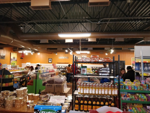 A busy grocery store interior with shelves stocked with various food items and customers shopping.