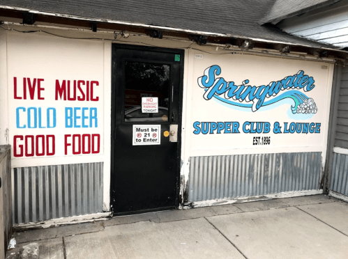 Entrance to Springwater Supper Club & Lounge, featuring signs for live music, cold beer, and good food.