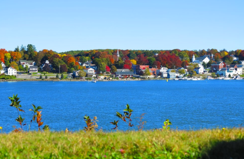 A vibrant autumn landscape featuring colorful trees along a calm lake, with a quaint town in the background.