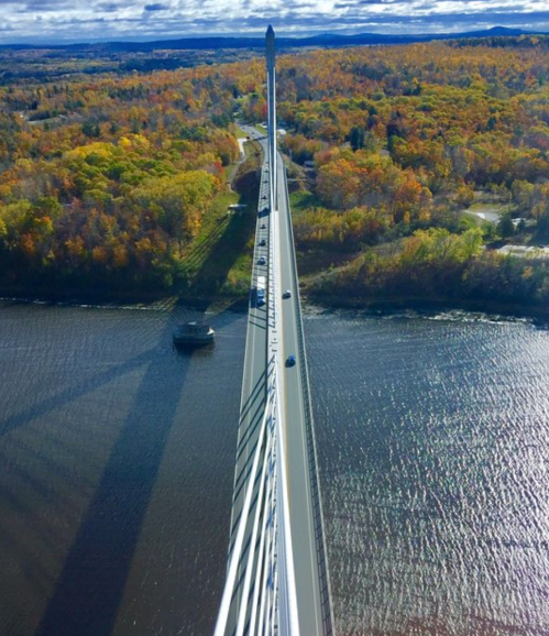 Aerial view of a bridge spanning a river, surrounded by vibrant autumn foliage and a shadow cast on the water.