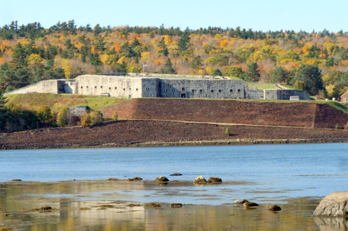 Historic stone fort on a hillside, surrounded by autumn foliage and a calm body of water.