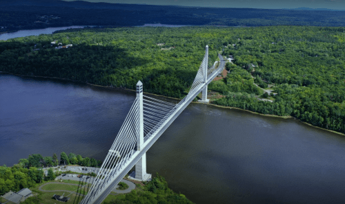 Aerial view of a cable-stayed bridge spanning a river, surrounded by lush green forests and hills.