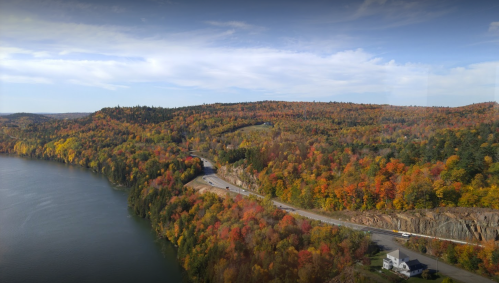 A scenic view of a winding road along a river, surrounded by vibrant autumn foliage and rolling hills.