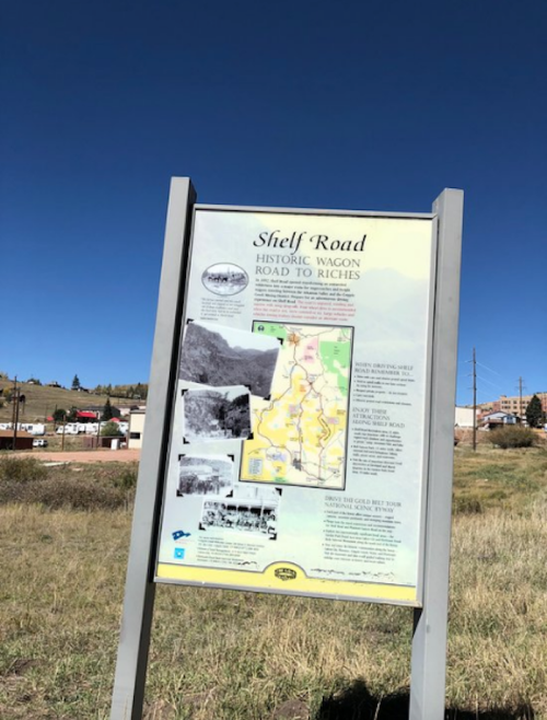 Sign for Shelf Road, detailing the historic wagon route with a map and historical photos, set against a clear blue sky.