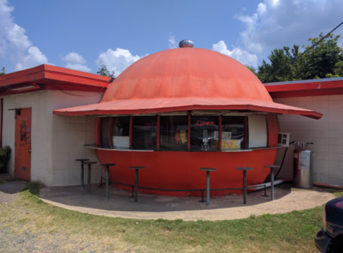 A small, round, red building with a dome roof and a counter, featuring stools outside and an "Open" sign.
