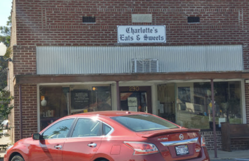 A red car parked in front of a brick building with a sign for "Charlotte's Eats & Sweets."