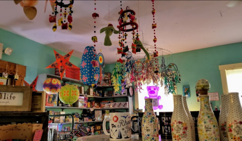 Colorful crafts and decorations hang from the ceiling in a vibrant shop filled with various artistic items and gifts.